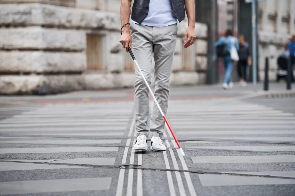 Low view of person with vision impairment cane walking through crosswalk.
